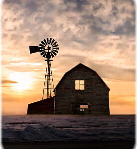 horizontal image of a an old abandoned farm house and barn looking desolate with a beautiful ornage sunset looming in the background on a cold winter evening..